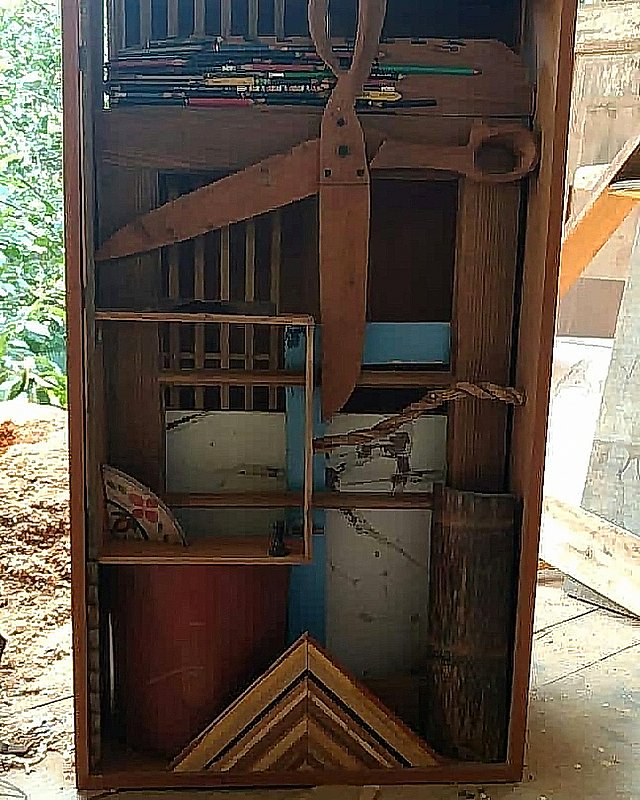 A obra Caixa (estudo) reúne tábuas, compartimentos e uma tesoura de madeira em montagem vertical dentro da oficina.