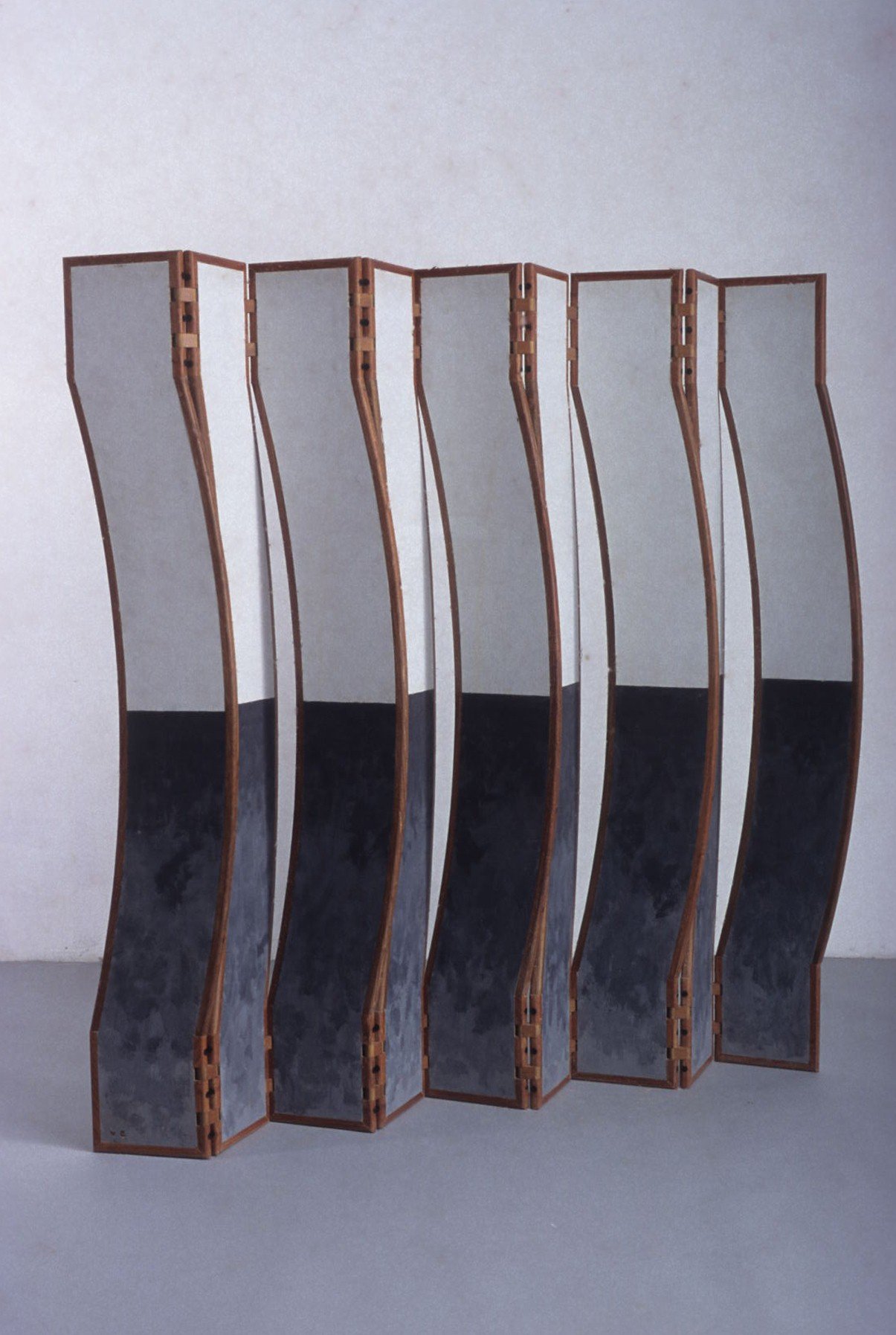 Escultura móvel com painéis verticais sinuosos divididos em metades branca e preta apoiada sobre o piso.