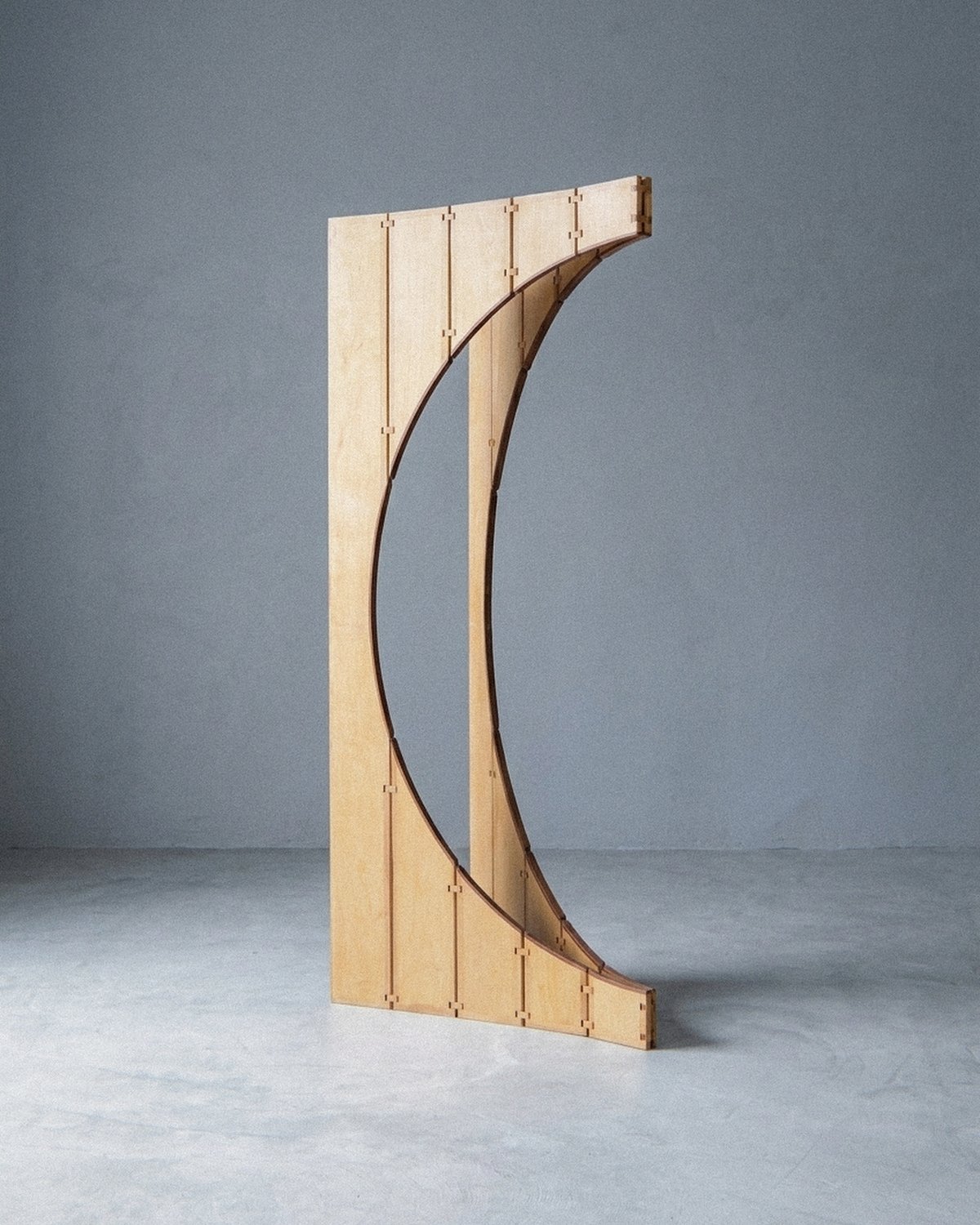 A escultura móvel Ó aberta em meia lua sobre piso de concreto diante de parede cinza clara.