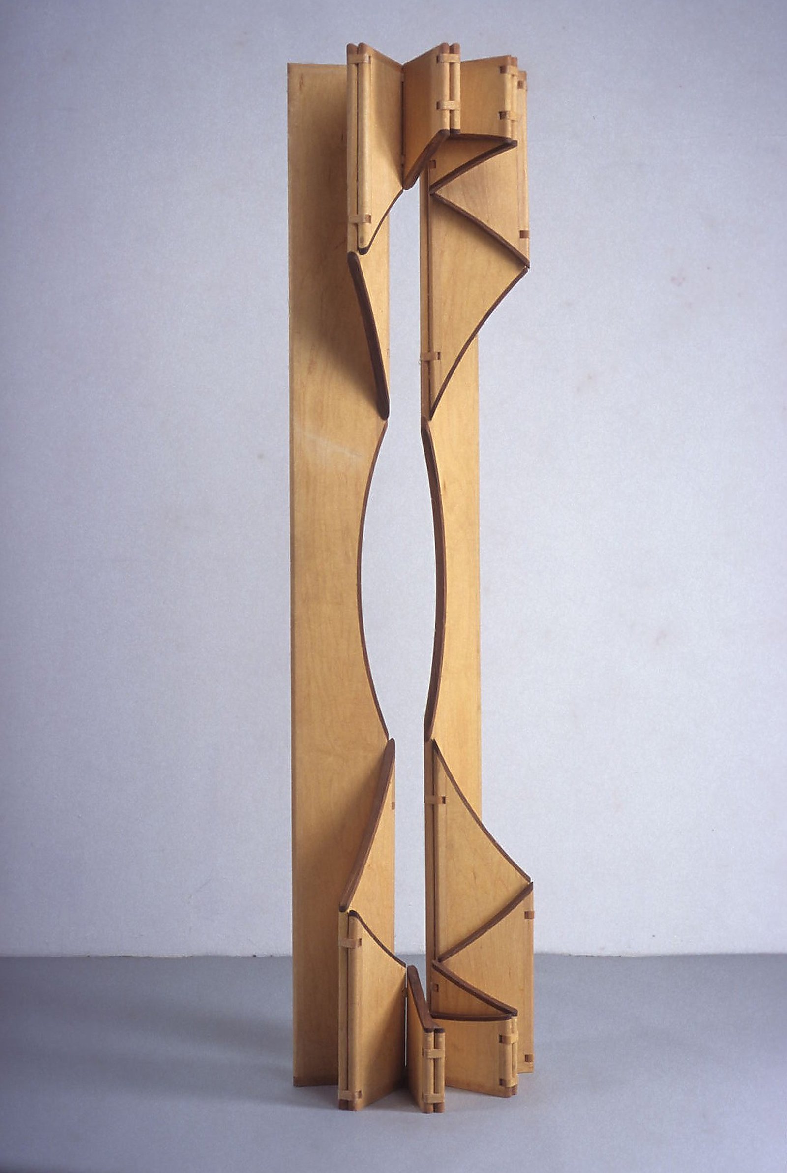 A escultura móvel Ó parcialmente aberta em painéis articulados de maple e freixo sobre fundo neutro.