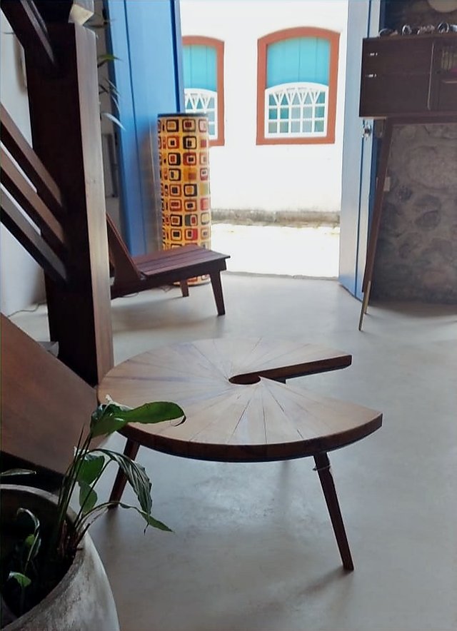 Mesa Caracol de madeira de recuperação em primeiro plano no interior de uma sala com piso claro.