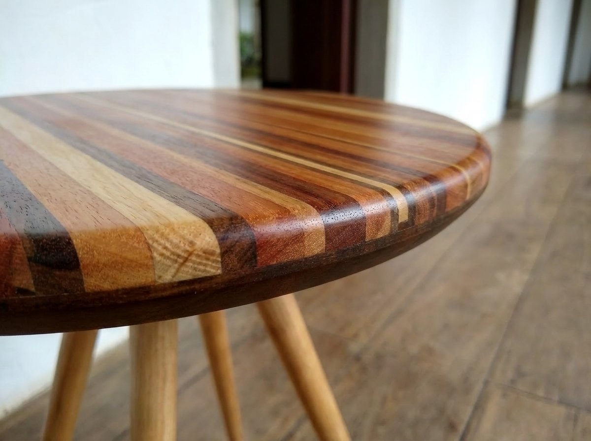 Detalhe oblíquo do tampo circular ripado da Mesa Donzela, mostrando as emendas de madeira sobre assoalho de tábuas.