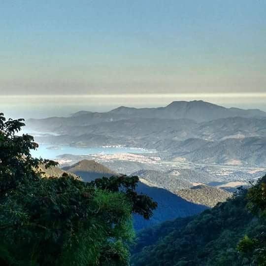 Vista panorâmica das montanhas arborizadas com o mar e a costa ao fundo sob céu claro.