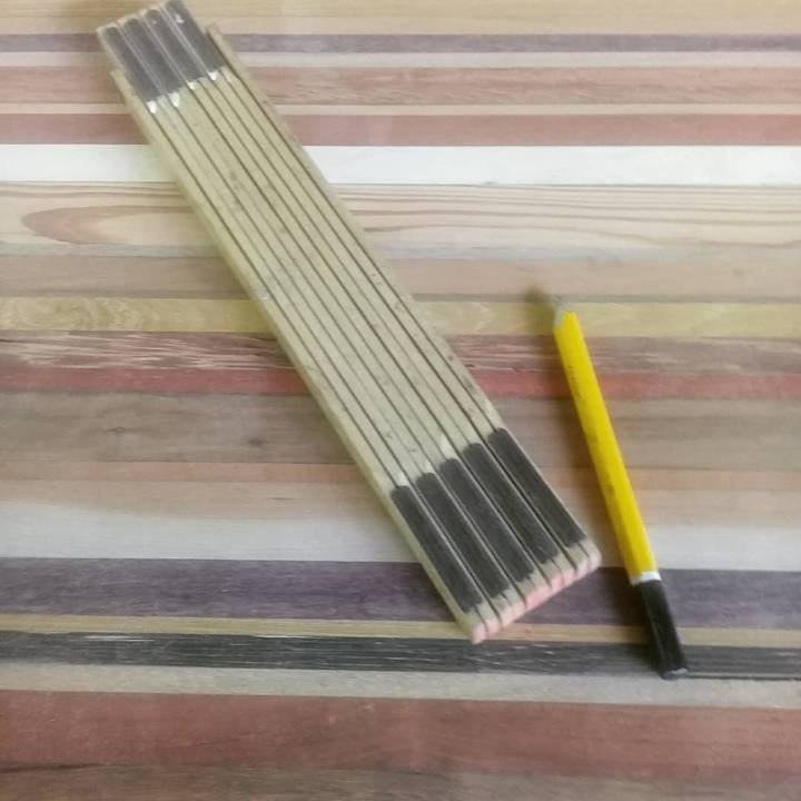 Um metro articulado de madeira fechado e um lápis amarelo sobre uma superfície de réguas coloridas.