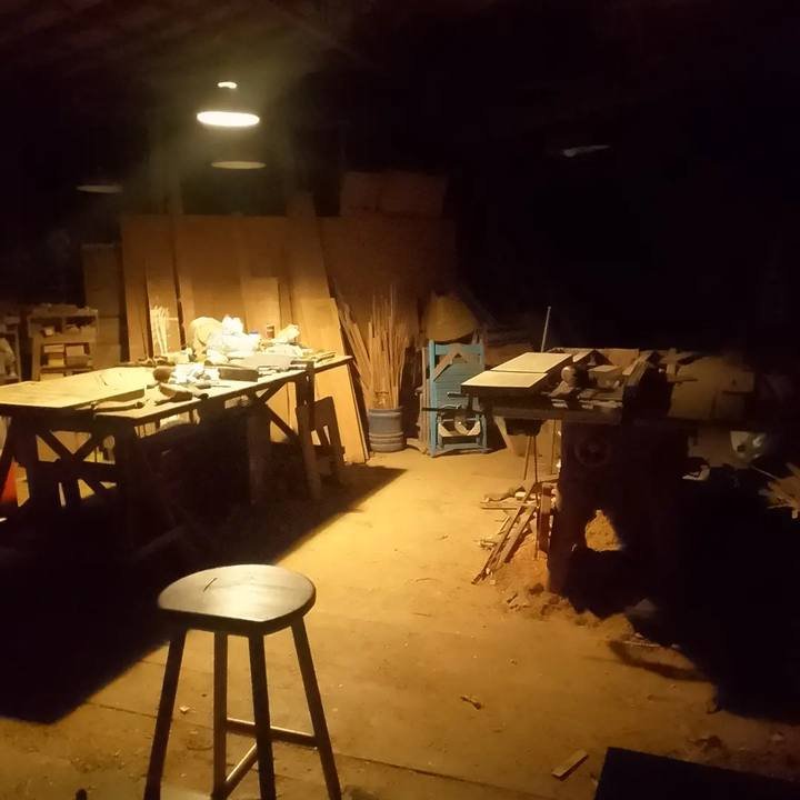 A oficina à noite com foco de luz sobre bancada de trabalho, ferramentas e banco alto.