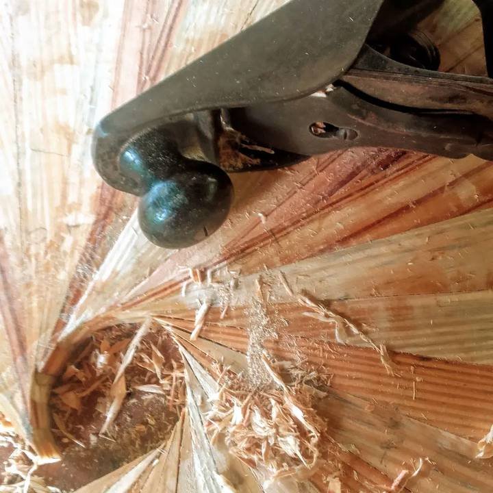 Uma plaina manual trabalhando sobre madeira com aparas e serragem ao redor do corte radial.