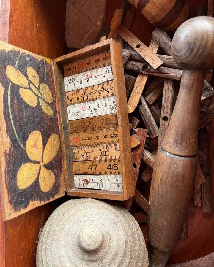 Gaveta aberta com pequenos pedaços de madeira, uma caixa com réguas dobradas e peças torneadas.