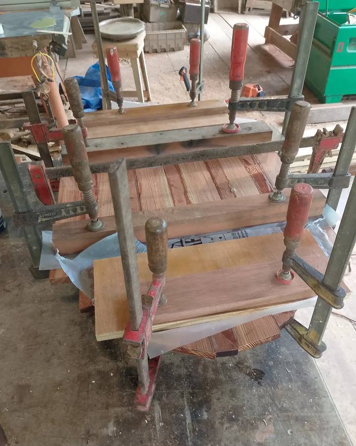 Ripas de madeira prensadas com grampos de aperto sobre uma bancada na oficina.