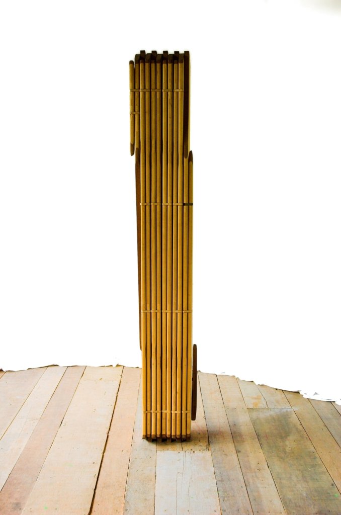 A escultura móvel Onda fechada em uma coluna vertical estreita sobre piso de tábuas de madeira.