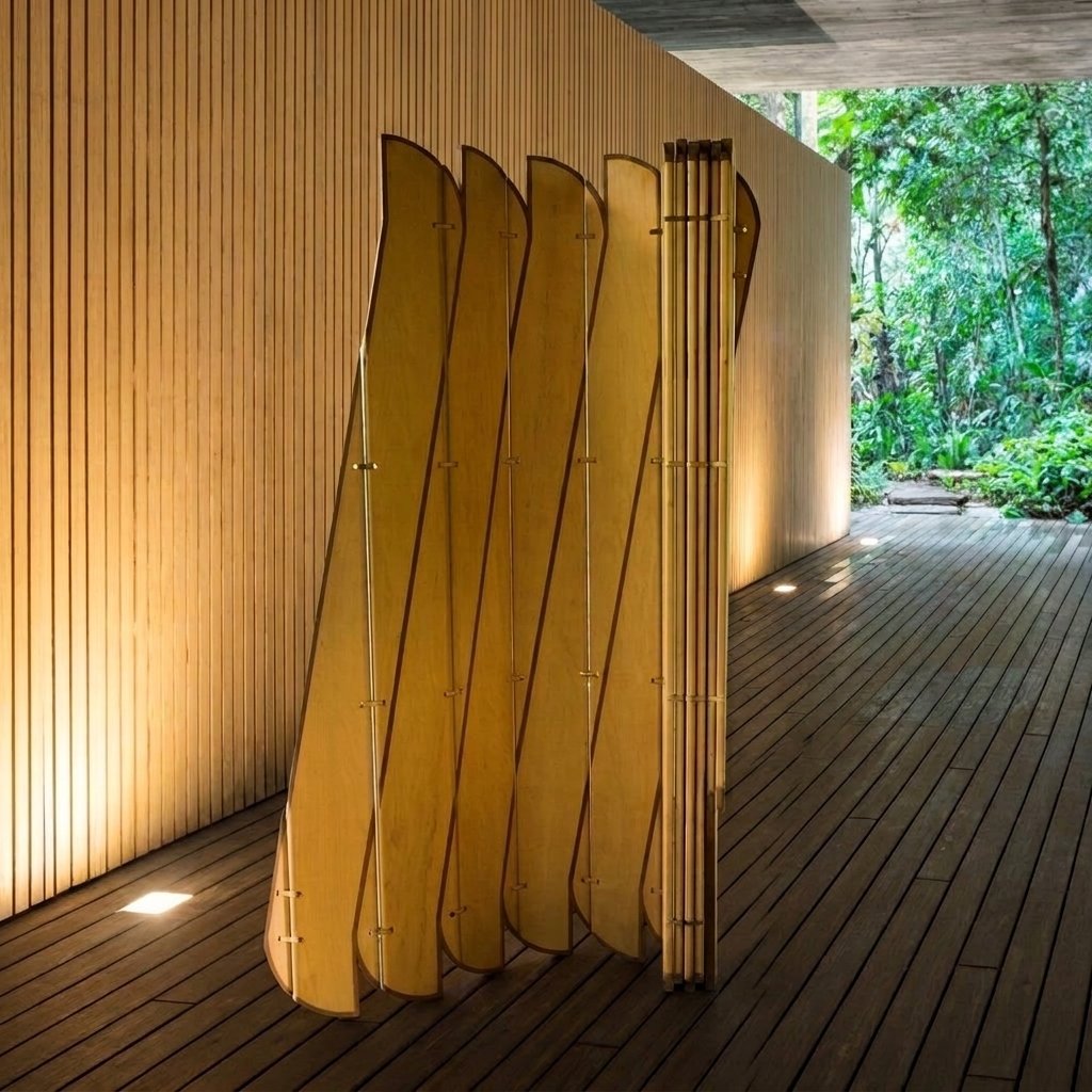 A escultura móvel Onda posicionada sobre deque de madeira ao lado de uma parede ripada com vista para árvores.
