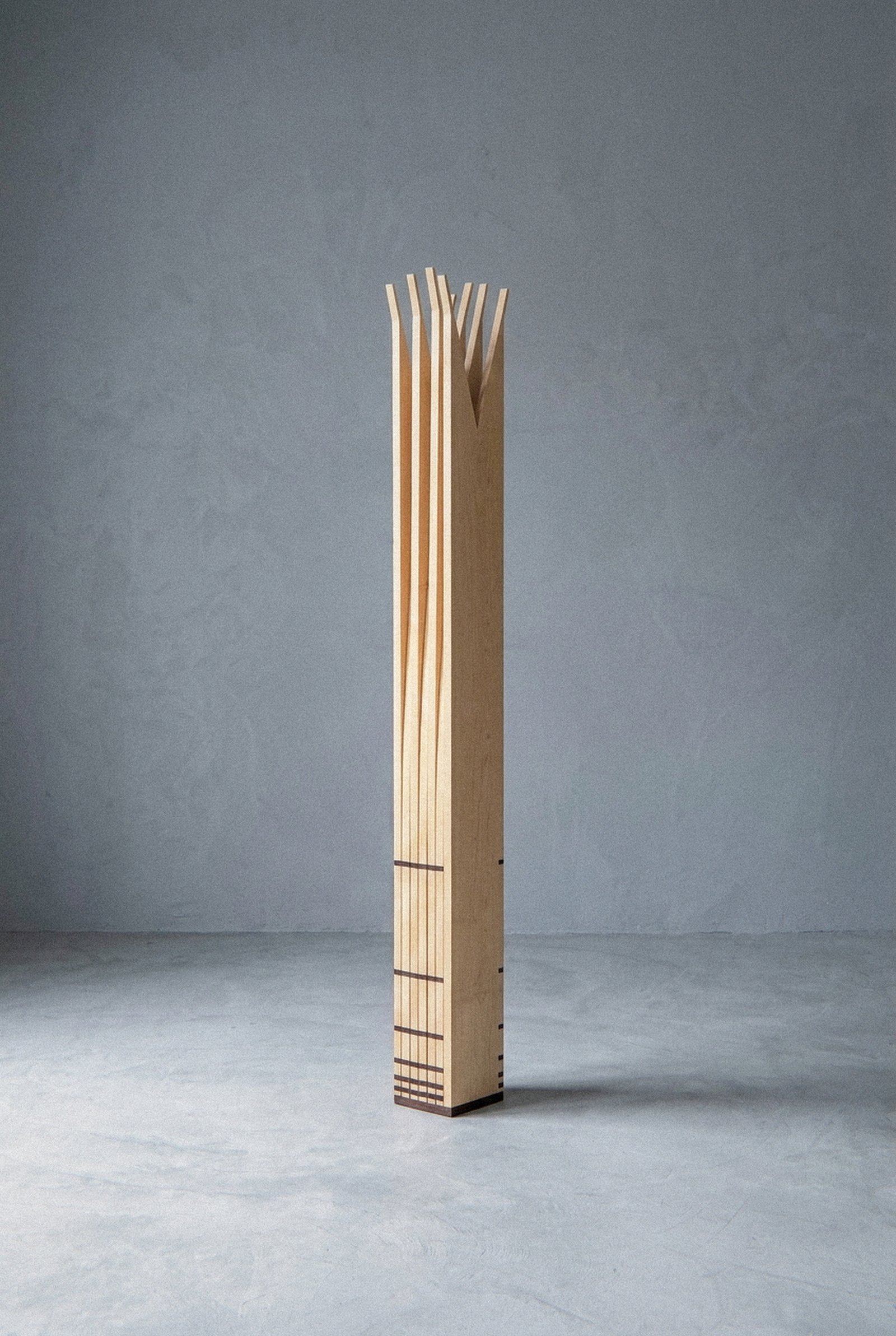 A escultura móvel Velas vista inteira e fechada como monólito colunar estreito sobre piso cinza claro.