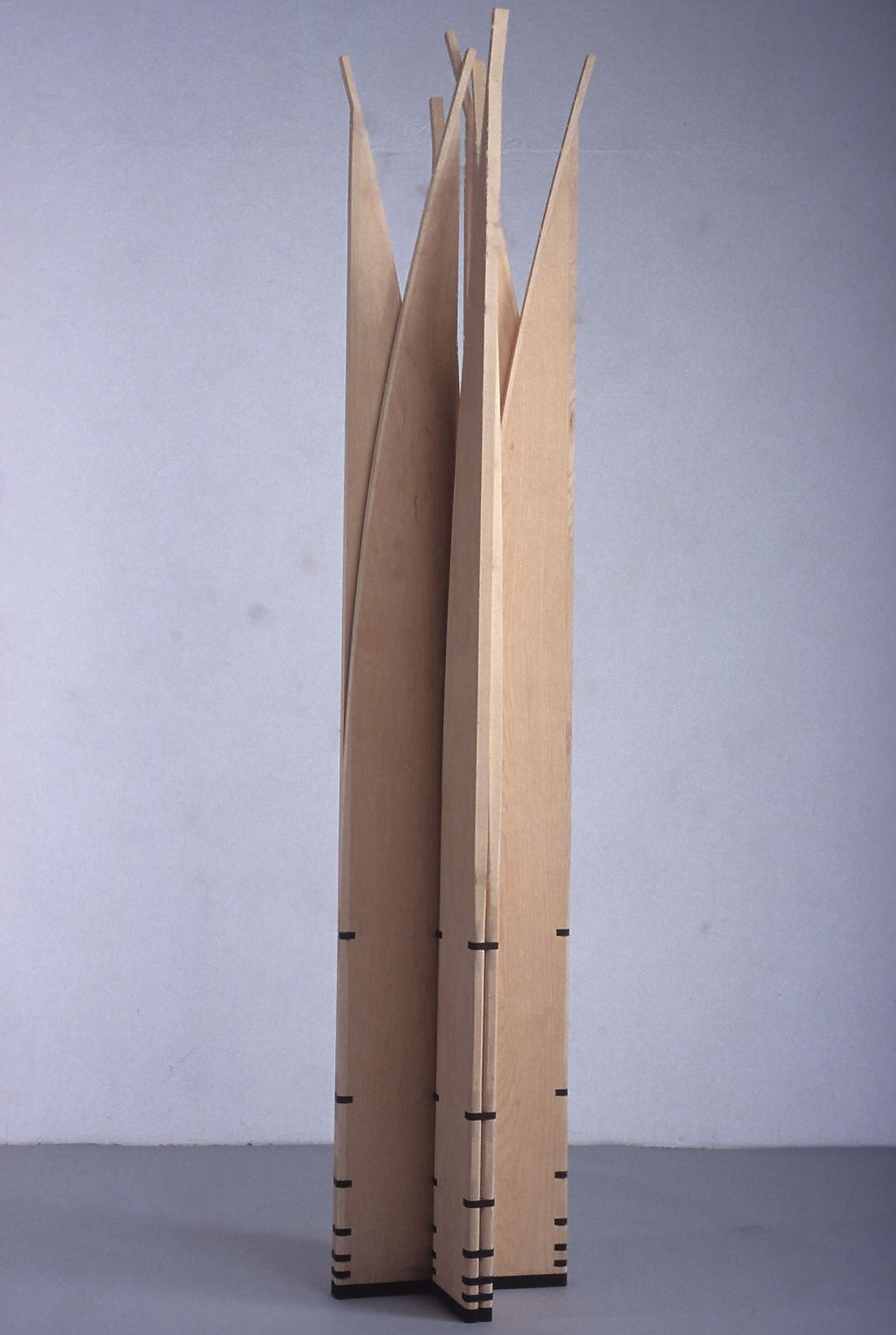 Fotografia da escultura móvel Velas aberta em perfil de coluna estelar, com hastes esguias erguidas diante de fundo cinza.